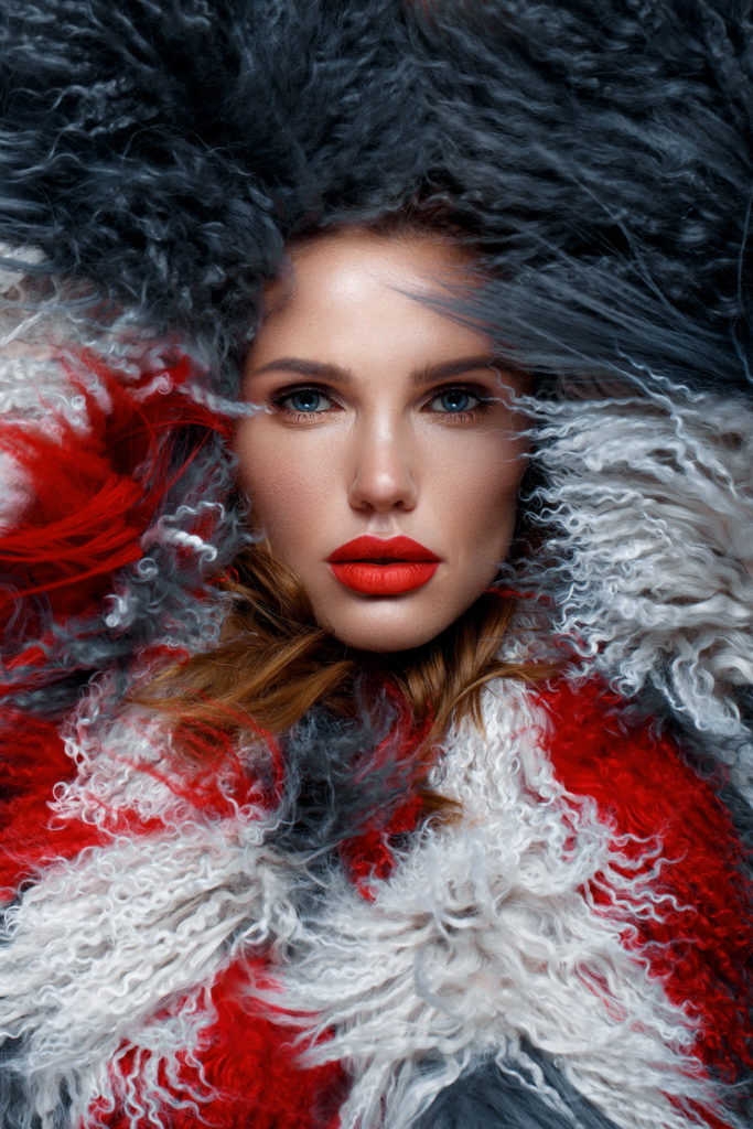 Beautiful woman with classic holiday make-up, red lips, curls in a multi-colored llama coat. Beauty face. Photo taken in studio